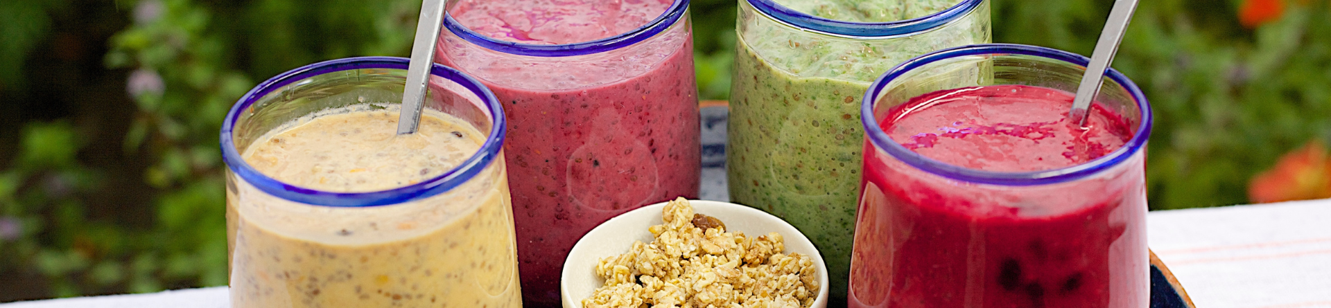 Quattro frullati colorati con ciotola di granola, serviti all'aperto.